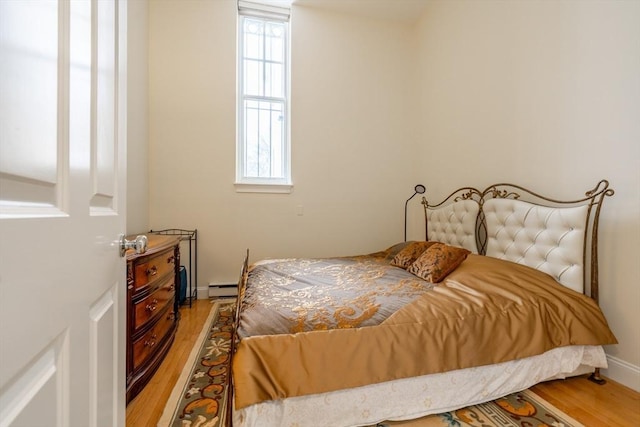 bedroom featuring wood finished floors, a baseboard heating unit, and baseboards