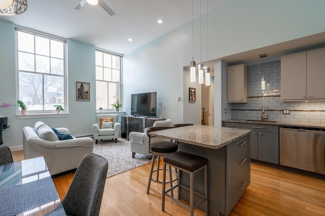 kitchen with stainless steel dishwasher, gray cabinets, a sink, a kitchen island, and open floor plan