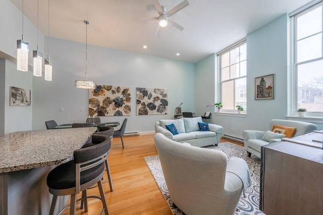 living area featuring baseboard heating, light wood-style flooring, a ceiling fan, baseboards, and recessed lighting
