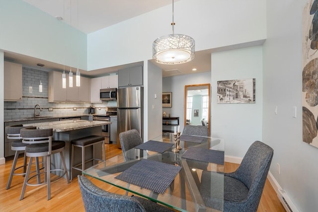 dining area with a baseboard heating unit, light wood-style floors, baseboards, and a towering ceiling