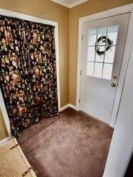 entryway with crown molding and dark carpet