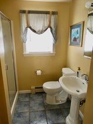 bathroom featuring walk in shower, toilet, and a baseboard heating unit