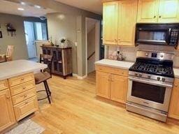 kitchen with light brown cabinets, stainless steel gas range, a kitchen bar, and light hardwood / wood-style floors