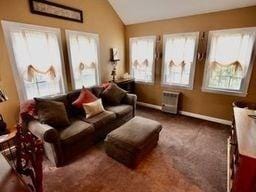 sitting room with dark carpet, a wall mounted AC, and vaulted ceiling