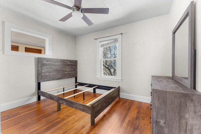 bedroom with baseboards, hardwood / wood-style floors, a ceiling fan, and ornamental molding