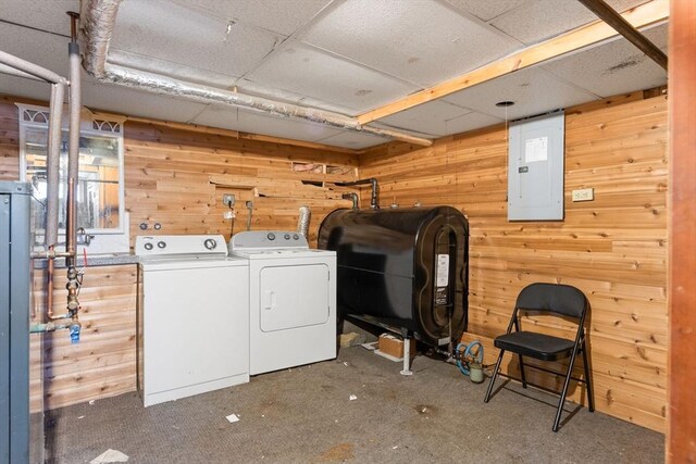 clothes washing area featuring wooden walls, laundry area, electric panel, heating fuel, and washer and dryer
