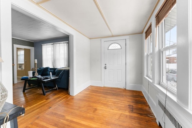 foyer with crown molding, radiator heating unit, light wood-style floors, and baseboards