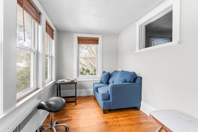 living area with baseboards, a textured ceiling, wood finished floors, and radiator heating unit
