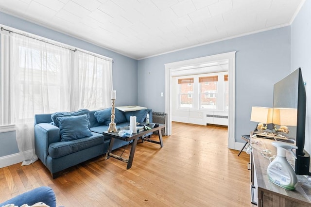 living room featuring baseboards, radiator, ornamental molding, and light wood finished floors