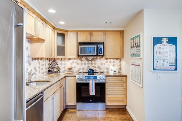 kitchen featuring a sink, light brown cabinetry, light stone countertops, backsplash, and stainless steel appliances