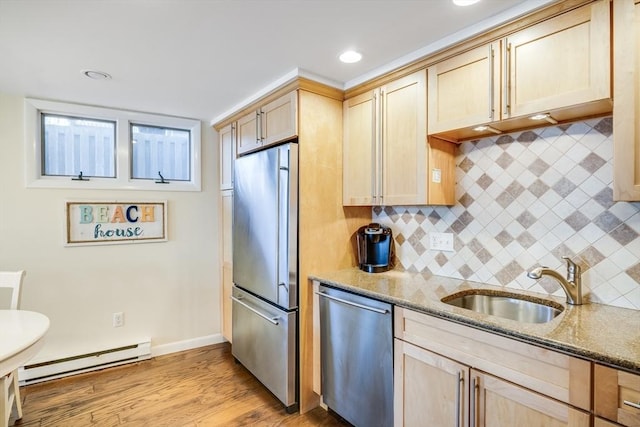 kitchen with light brown cabinets, light stone counters, stainless steel appliances, a baseboard radiator, and a sink
