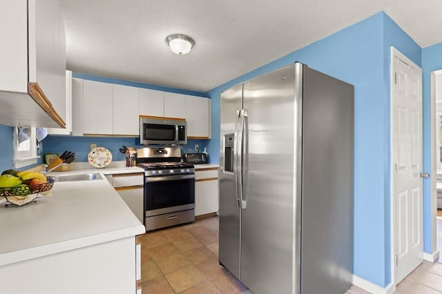 kitchen featuring a toaster, light countertops, white cabinetry, a textured ceiling, and appliances with stainless steel finishes
