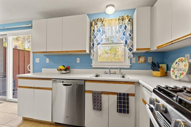 kitchen with appliances with stainless steel finishes, white cabinetry, light countertops, a sink, and light tile patterned flooring