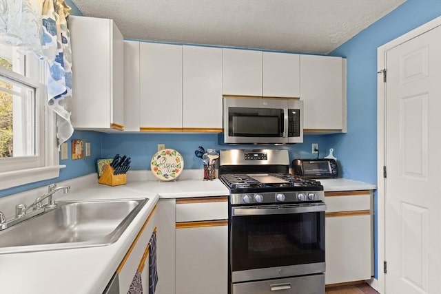 kitchen featuring a sink, appliances with stainless steel finishes, white cabinets, and light countertops