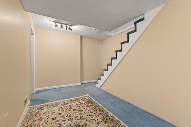 finished below grade area featuring baseboards, carpet flooring, stairs, and rail lighting