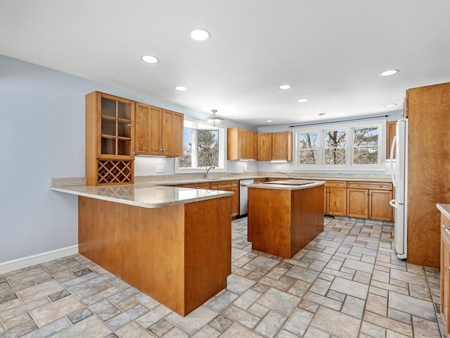 kitchen featuring a peninsula, glass insert cabinets, brown cabinets, and freestanding refrigerator