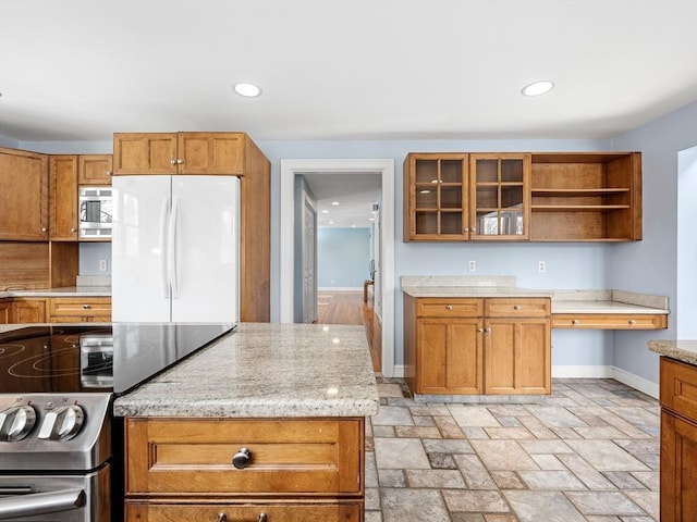 kitchen featuring built in study area, glass insert cabinets, appliances with stainless steel finishes, light stone countertops, and open shelves