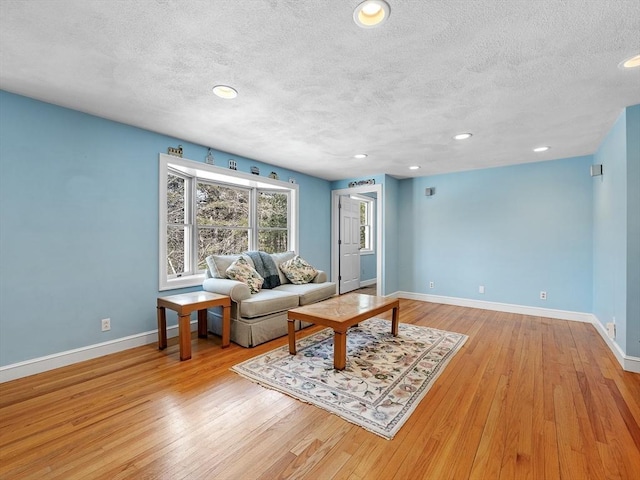 living room featuring light wood-style floors, baseboards, a textured ceiling, and recessed lighting