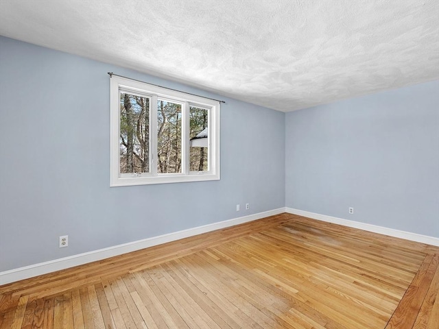 spare room with a textured ceiling, hardwood / wood-style floors, and baseboards