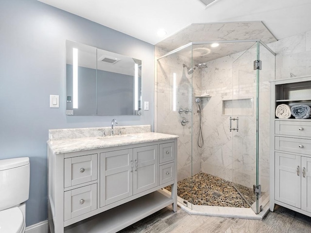 bathroom with toilet, wood finished floors, visible vents, vanity, and a stall shower