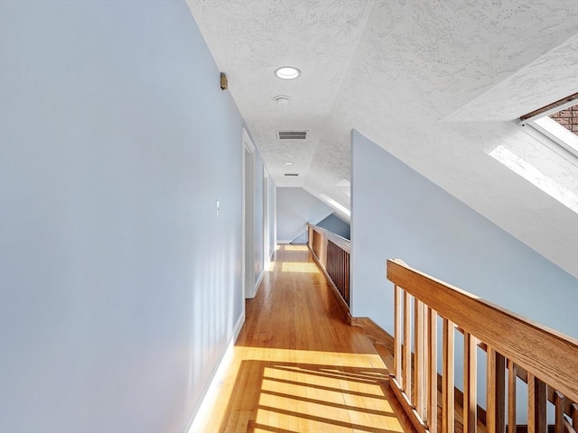 corridor featuring light wood-style floors, visible vents, and a textured ceiling