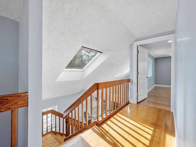 corridor featuring a textured ceiling, vaulted ceiling with skylight, hardwood / wood-style flooring, and baseboards