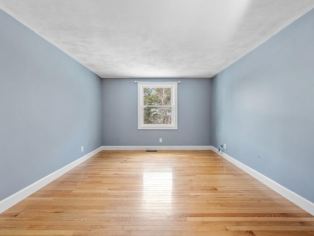 spare room featuring light wood-style flooring, visible vents, baseboards, and a textured ceiling