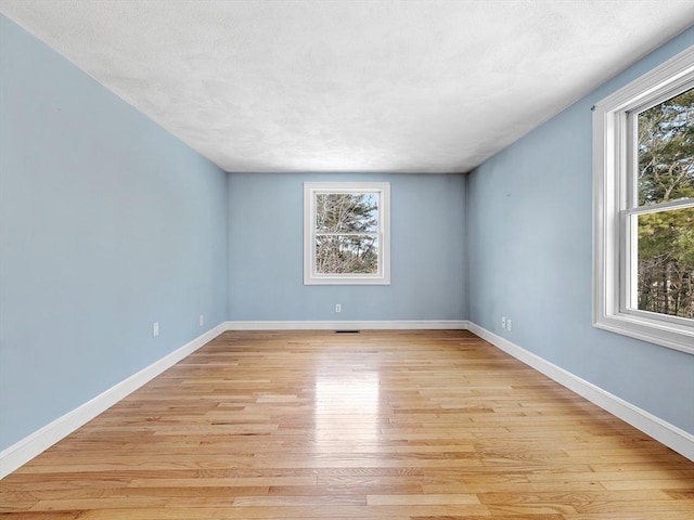 empty room featuring baseboards, plenty of natural light, and light wood-style floors