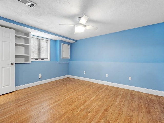 spare room featuring ceiling fan, a textured ceiling, visible vents, baseboards, and light wood-style floors