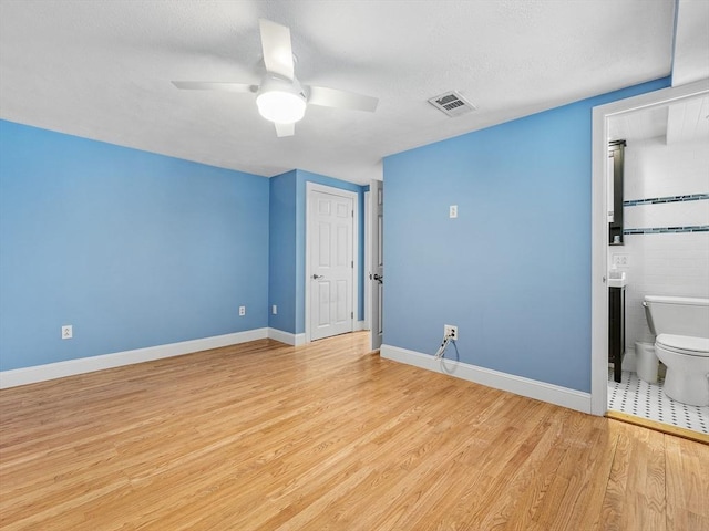 unfurnished bedroom featuring ceiling fan, light wood-style flooring, visible vents, baseboards, and ensuite bath