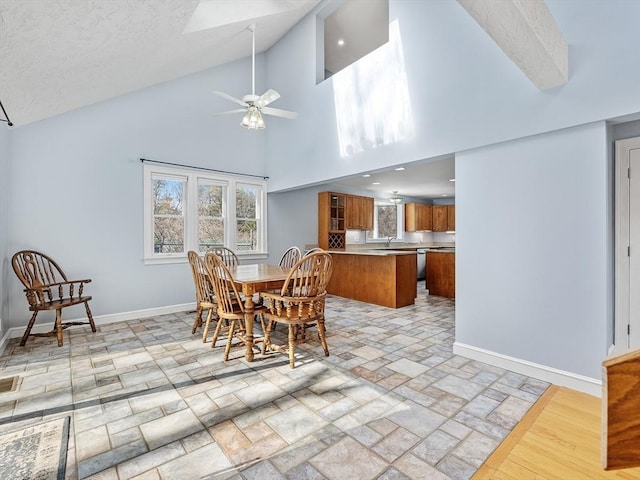 dining area featuring ceiling fan, high vaulted ceiling, stone finish floor, and baseboards