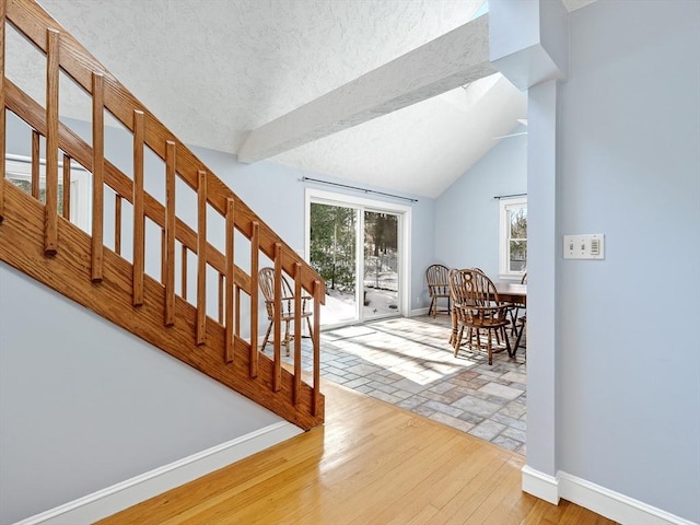 interior space with a textured ceiling, baseboards, stairway, light wood finished floors, and lofted ceiling with skylight