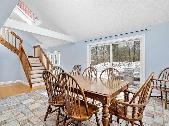 dining space with lofted ceiling with skylight, stone tile floors, baseboards, and stairs