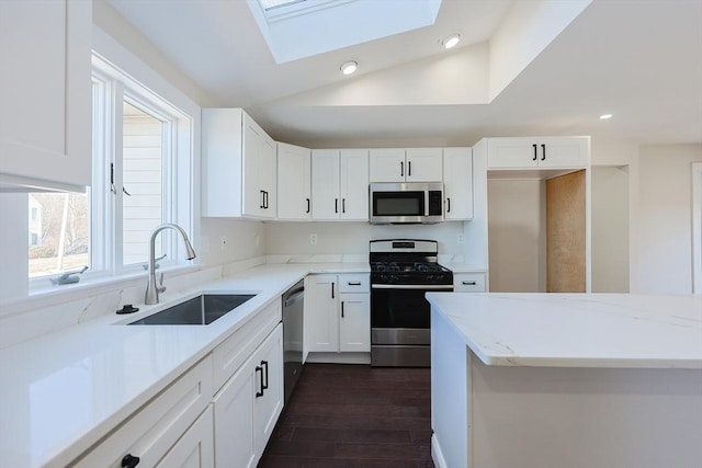 kitchen with stainless steel appliances, a sink, lofted ceiling, white cabinets, and a skylight