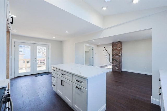 kitchen with french doors, white cabinets, dark wood-type flooring, light stone countertops, and a center island