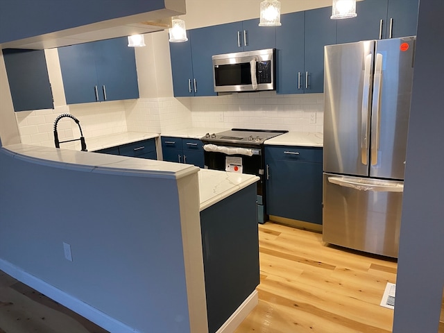 kitchen with decorative light fixtures, light hardwood / wood-style flooring, stainless steel appliances, blue cabinetry, and tasteful backsplash