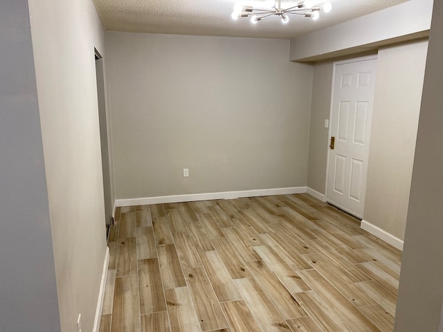 empty room featuring an inviting chandelier, a textured ceiling, and light hardwood / wood-style floors