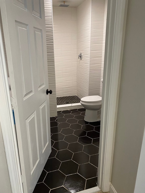 bathroom with toilet, tile flooring, and tiled shower