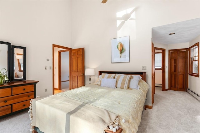 carpeted bedroom featuring a baseboard heating unit, a towering ceiling, and ceiling fan