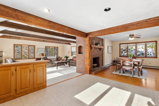 dining space featuring ceiling fan, a fireplace, a baseboard radiator, and beamed ceiling