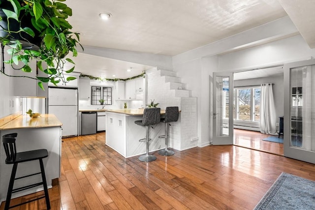 kitchen featuring a peninsula, freestanding refrigerator, white cabinets, stainless steel dishwasher, and light wood-type flooring