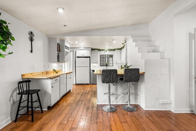 kitchen with a peninsula, freestanding refrigerator, white cabinets, a kitchen bar, and light wood-type flooring