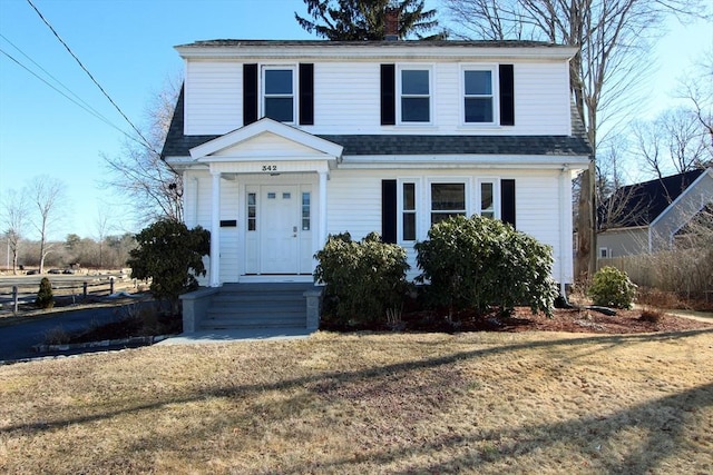 view of front of home with a shingled roof, a front lawn, and a chimney