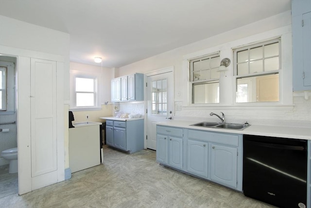 kitchen with blue cabinetry, light countertops, a sink, washer / dryer, and dishwasher