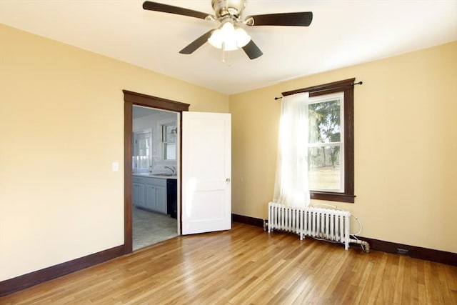 spare room with light wood-style floors, radiator, a sink, and baseboards