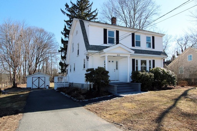 view of front of property with a shingled roof, a gambrel roof, a chimney, aphalt driveway, and an outbuilding