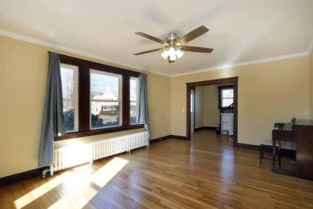 empty room featuring crown molding, radiator heating unit, wood finished floors, and baseboards