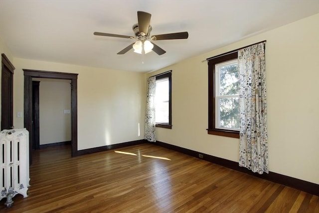 spare room featuring baseboards, dark wood-type flooring, a ceiling fan, and radiator