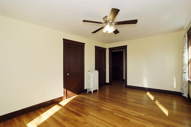 empty room featuring radiator heating unit, wood finished floors, a ceiling fan, and baseboards