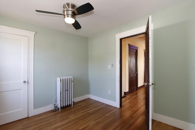 spare room featuring baseboards, wood finished floors, and radiator